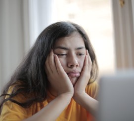 Grumpy, bored woman with her head in her hands looking at a computer screen.