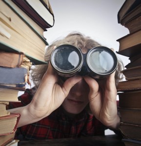 Person searching with binoculars in between two stacks of books