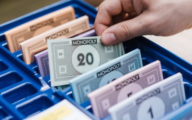 Bank from Monopoly. A hand grabs one of the neatly organized 20-dollar bills