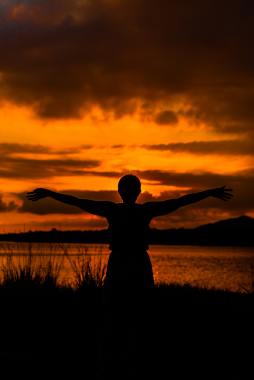 Triumphant woman silhouetted against an orange and vivid sunset
