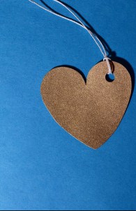 A sparkly gold heart on card stock with a piece of white string looped around it. The heart and string sit on a dark background