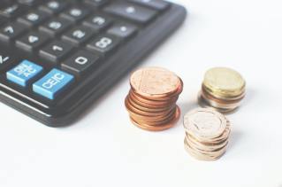 Three stacks of coins sit next to a partially visible black calculator with two blue buttons on it.