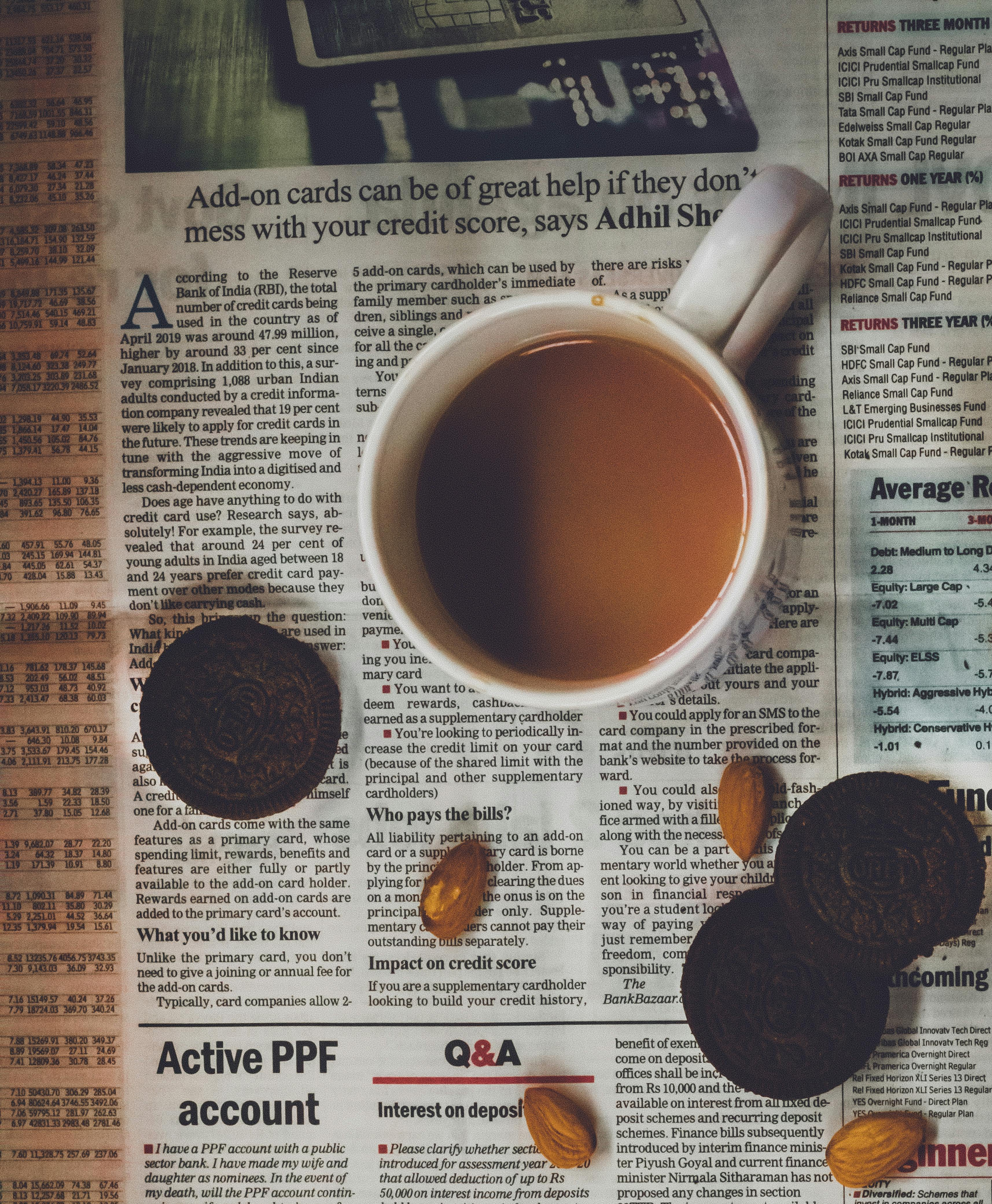 A cup of coffee, cookies, and almonds rest on a newspaper.