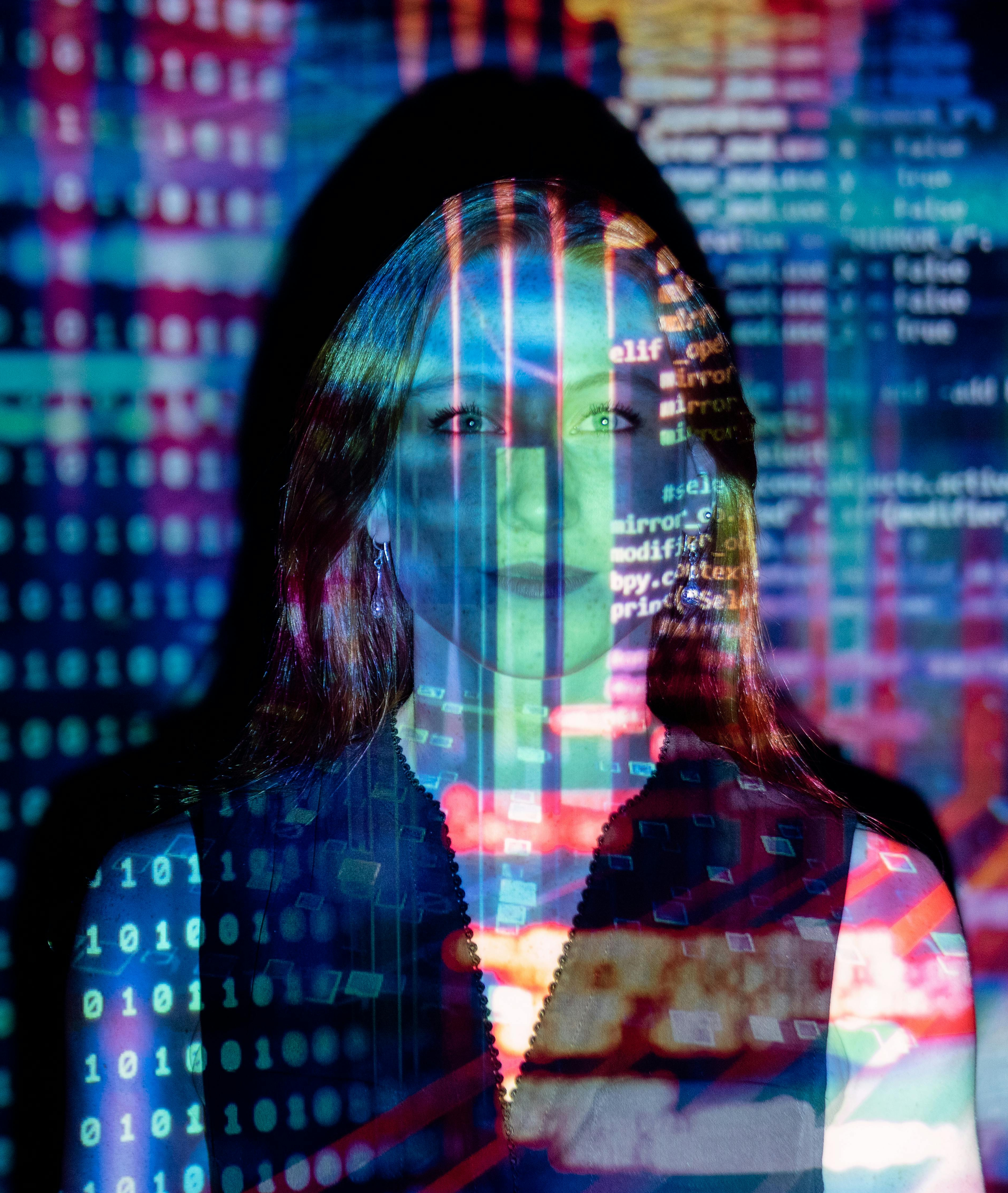 A woman stands in front of a screen with HTML code being projected over the screen and her.