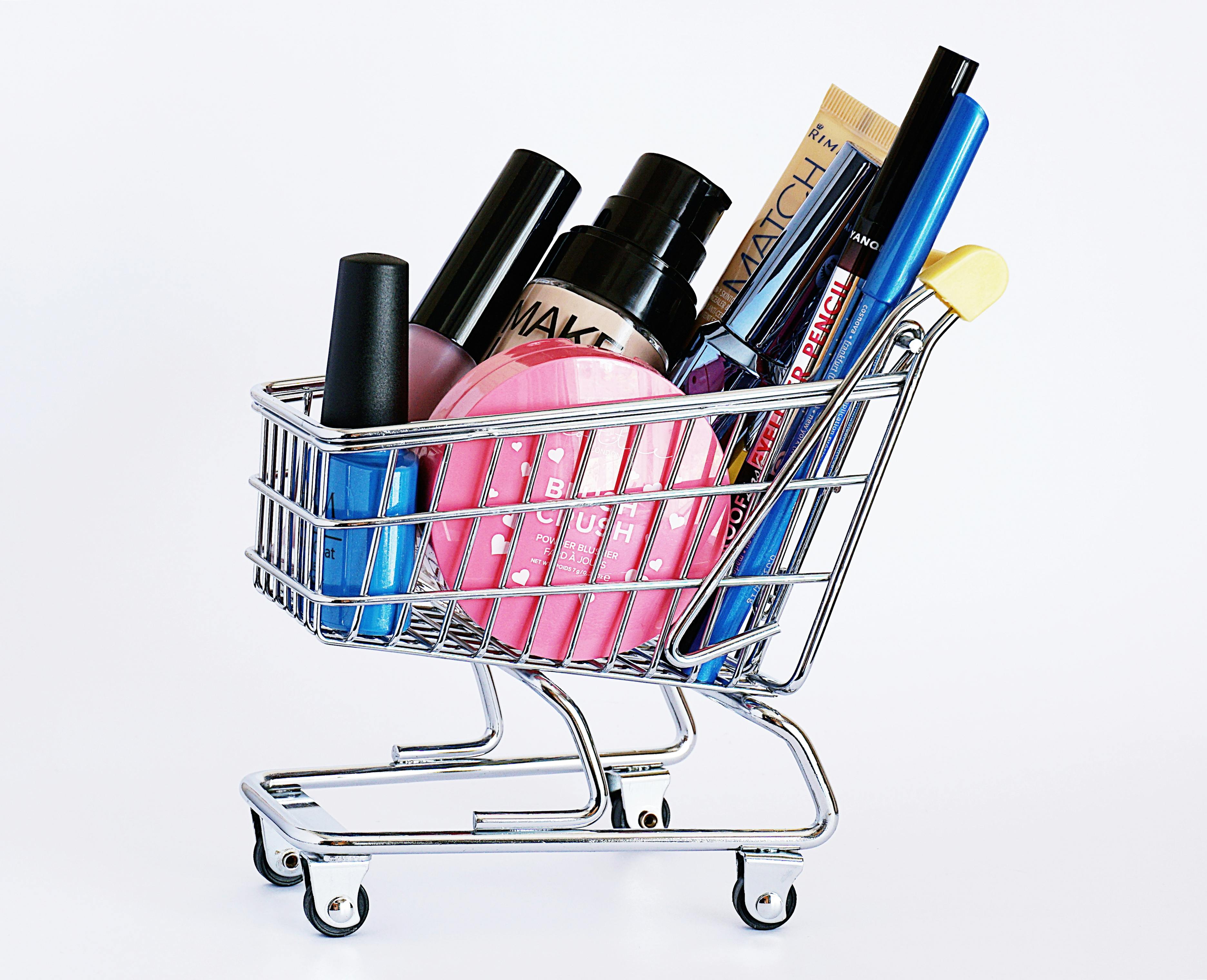 A selection of makeup and nail polish sit in a mini shopping cart with a yellow handle