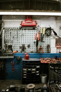 Picture is centred on a workmen's bench with various tools hanging. It is a industrial setting with am old-fashioned red oil can grabbing the eye.