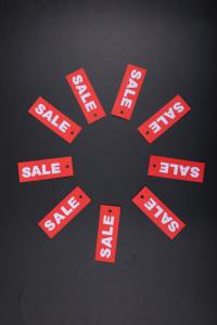 Ten red tags reading "SALE" are fanned out into a circle on a black tablecloth