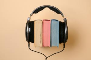 A brown book, a print book ,and a blue took sit with their colour-matching pages facing the camera. Wrapped around them is a pair of black studio headphones and a cord that runs down out of the frame.