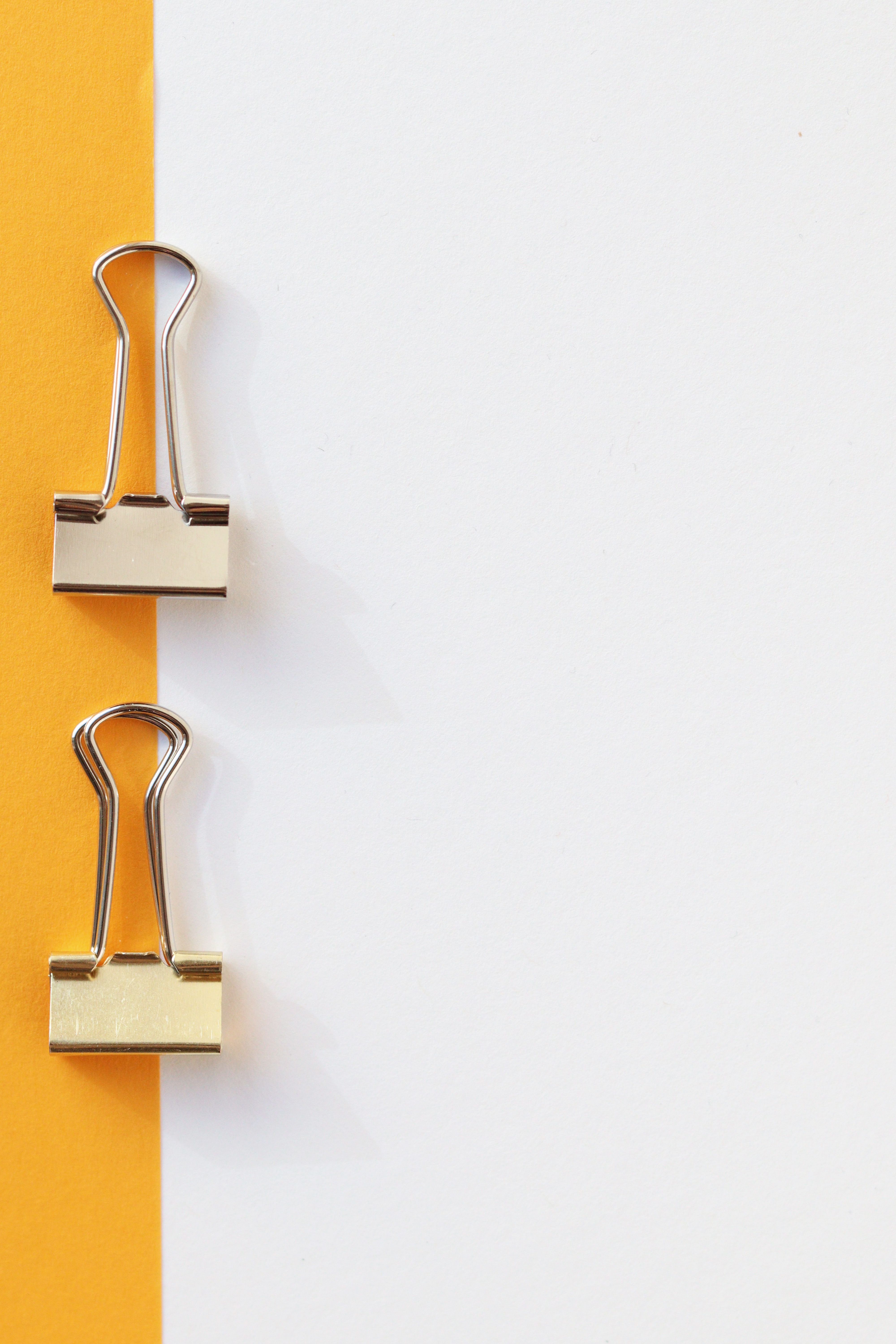 Two gold binder clips sit on a white piece of paper with a yellow border.