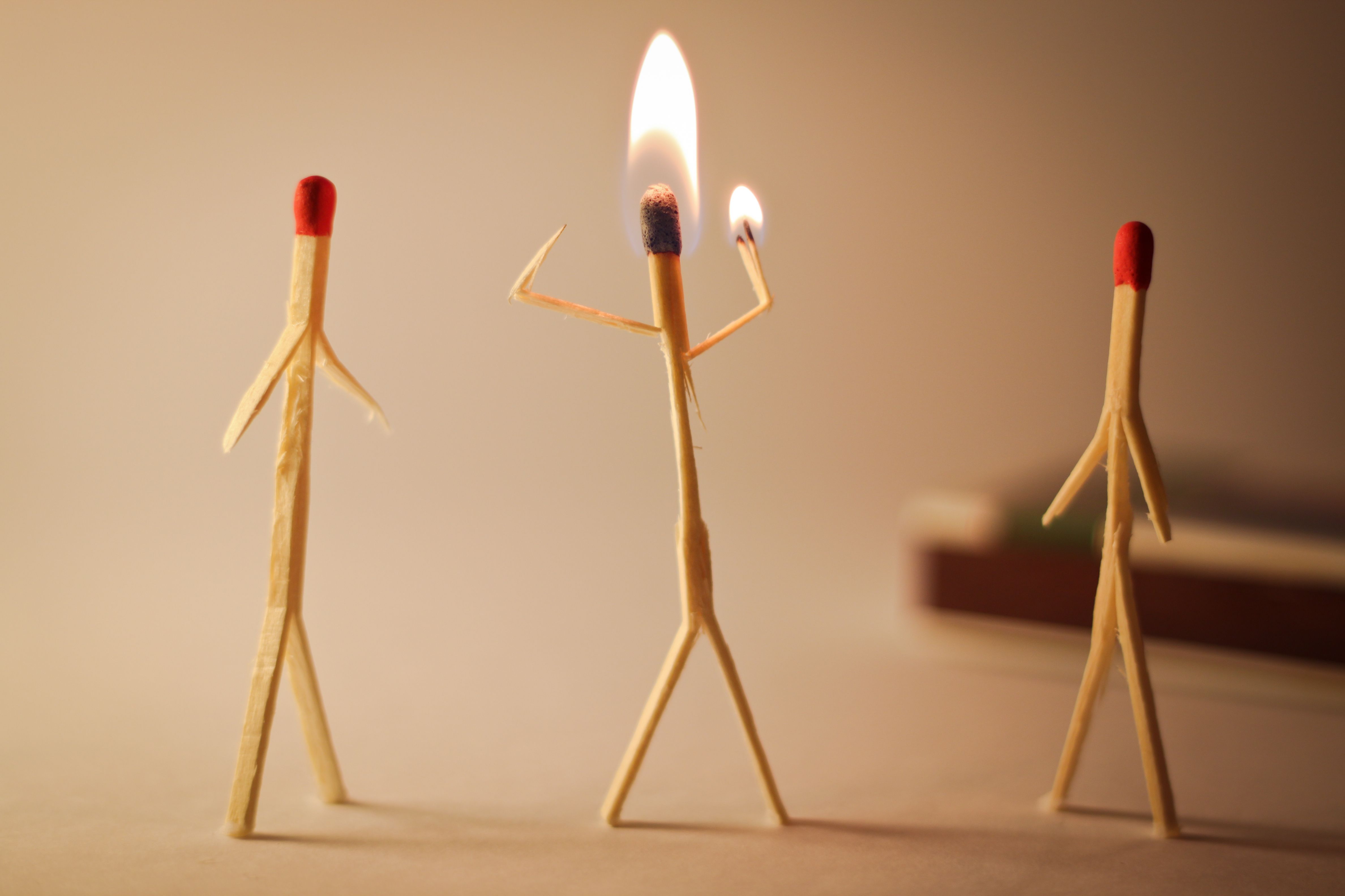 Three matches are stood up with arms to look like matchstick humans. The one in the middle is burning and the other two are unlit.