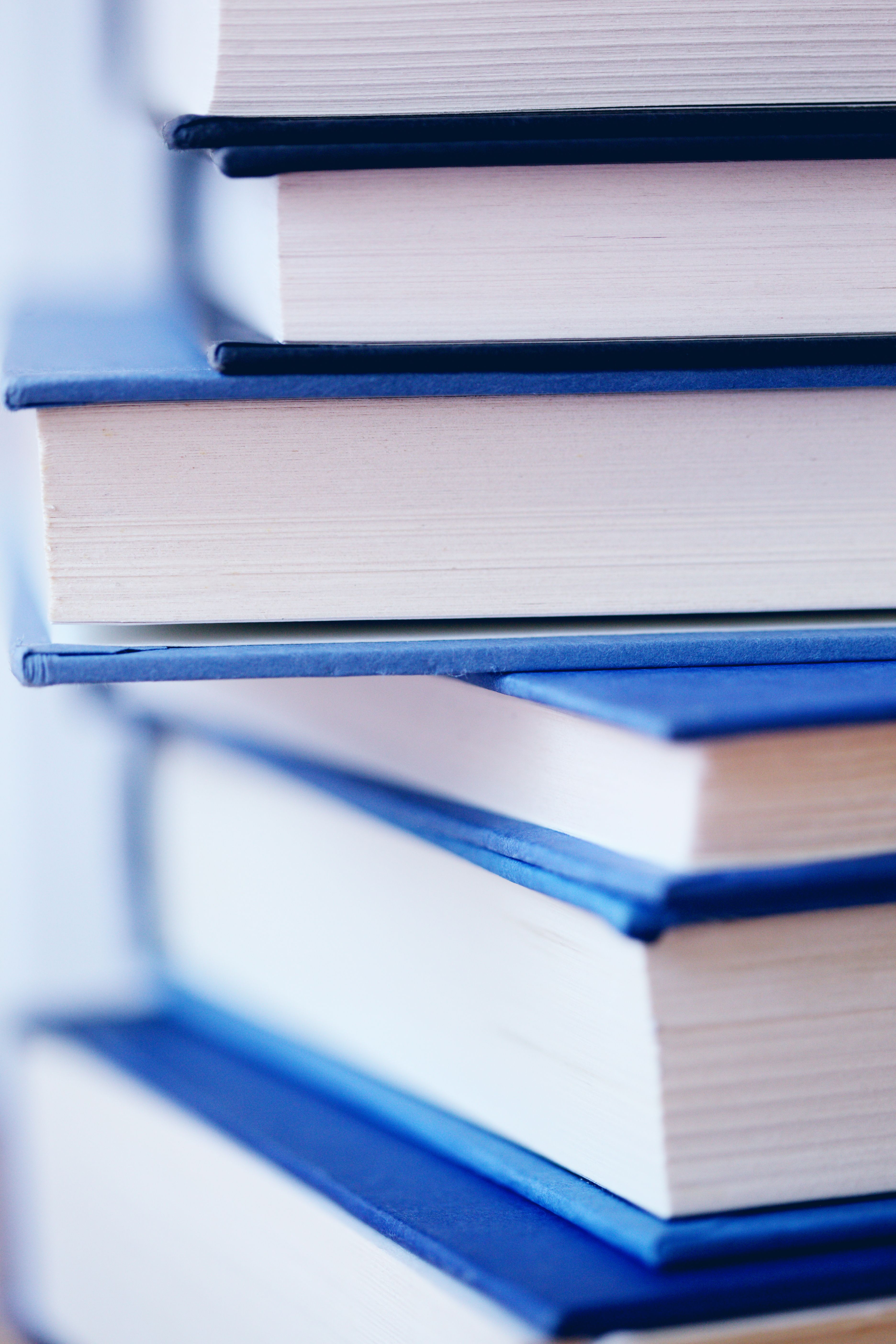 A pile of books with blue cover in varying shades are piled askew against a white blurred background