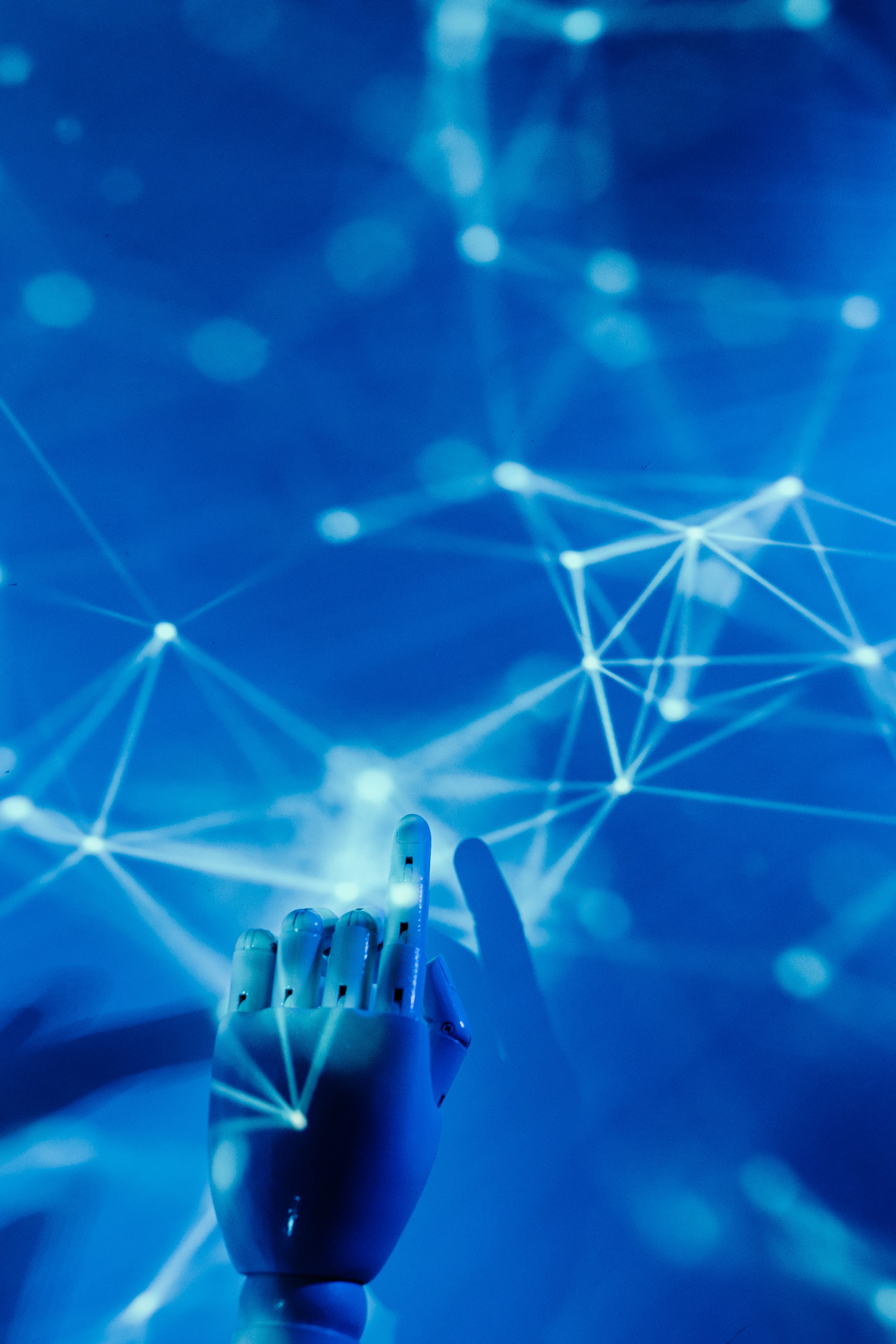 A neural network in blue shades is the background, implying AI and online network.  A robotic hand with a pointer hand stretched out is reaching for one of the nodes.