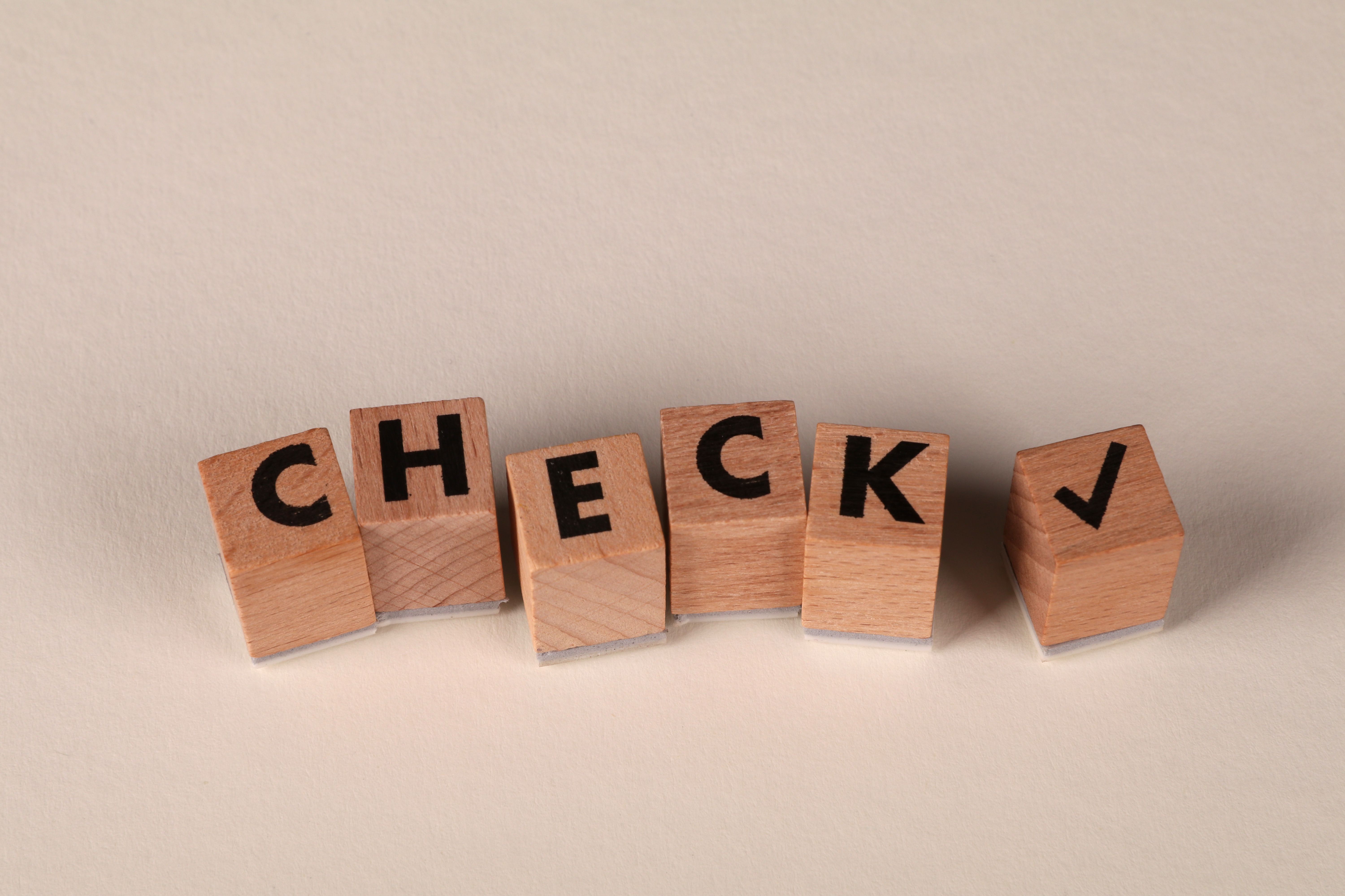 On a white table, wooden blocks with letters spell out "CHECKS" with a checkmark on the last block.