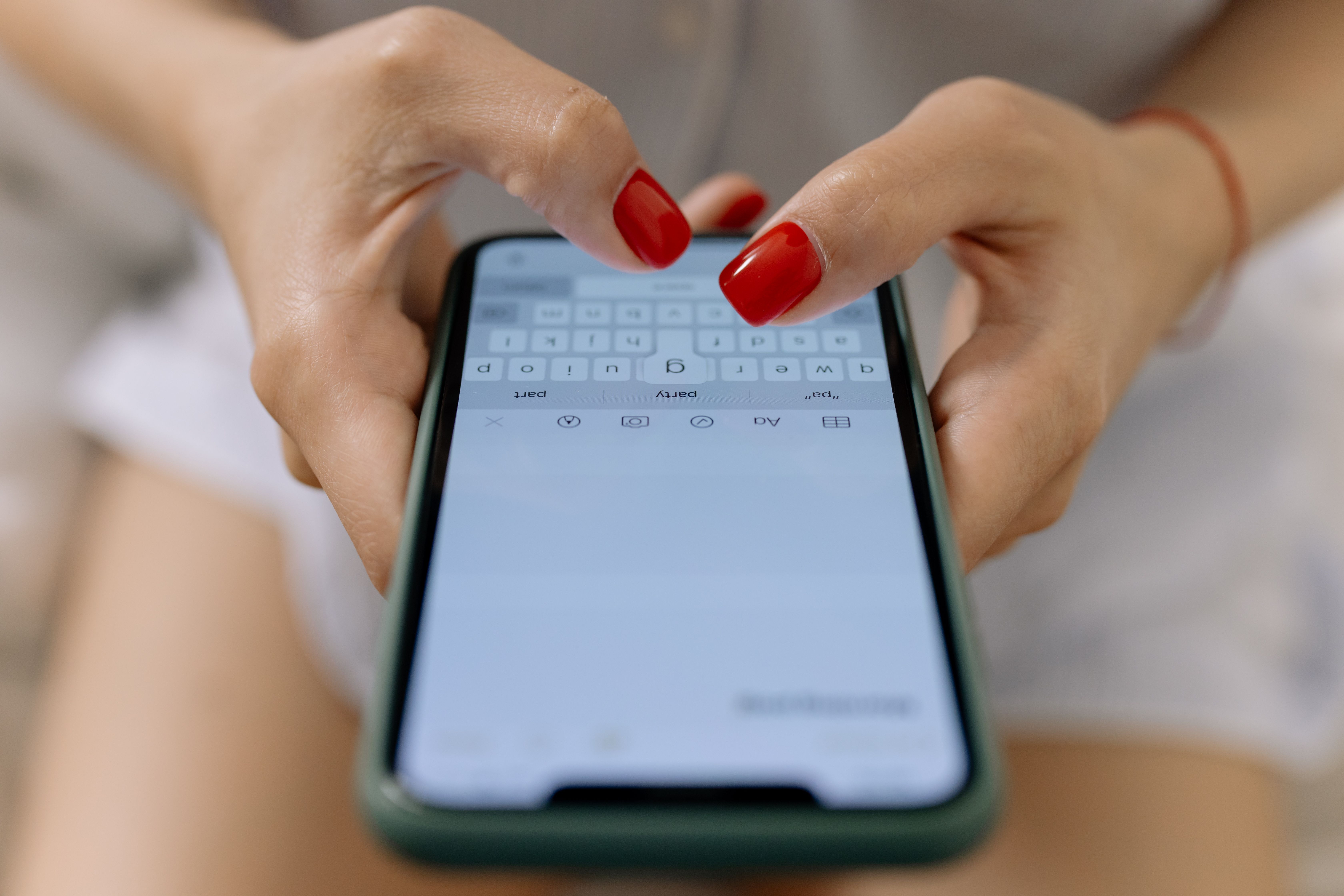 A woman with red fingernail polish is typing on an iPhone in the Notes app.